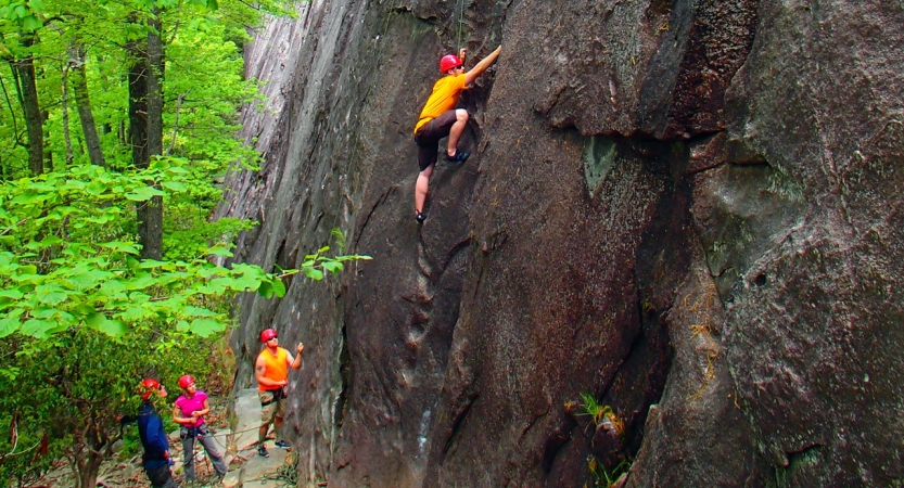 一个人穿着安全装置是由绳索爬岩墙。在地面上,一个人当别人看适用。