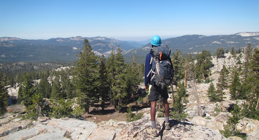 一个人戴着头盔和一个背包的面孔离相机,看起来就像巨大的多山的地形